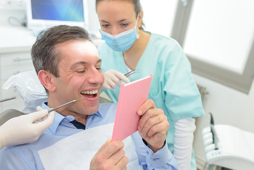 Male patient places a small mirror next to this face looking at his newly replaced dental crown