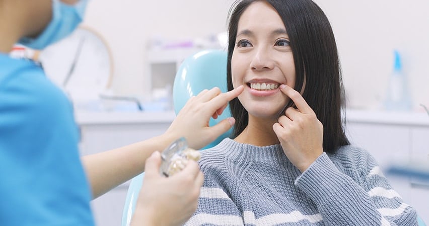 A young asian woman sits at the dentists office pointing to a loose tooth in her mouth. For kids, a loose tooth is something really exciting. It’s a sign of growing up, as baby teeth fall out and are replaced with full size grown up teeth. And, if they’re lucky, they may even get a little bonus from the Tooth Fairy.