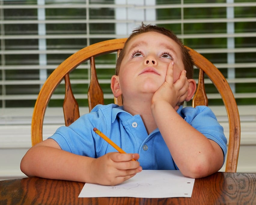 Thoughtful child doing his homework at kitchen table - Sometimes you explain dental implants like you would to a 5 year old