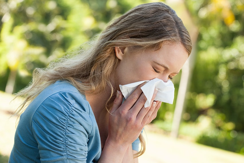 Young woman sneezing into a kleneex. While you might be sneezing this summer, those symptoms might be hiding your TMJ.