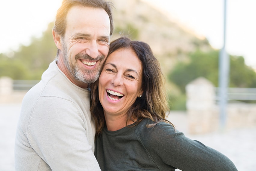 Romantic couple smiling and cuddling on a sunny day. If you’ve recently lost one or more teeth and feel embarrassed by the gaps in your smile, there is an answer: dental implants.