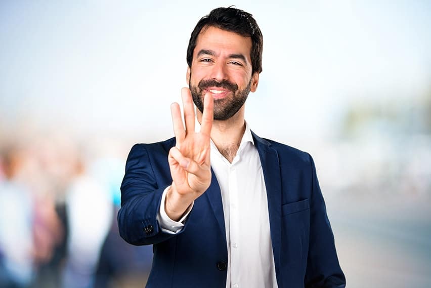 Professional business man holds up 3 fingers while showing off his smile. Here are the 3 benefits of dental veneers.
