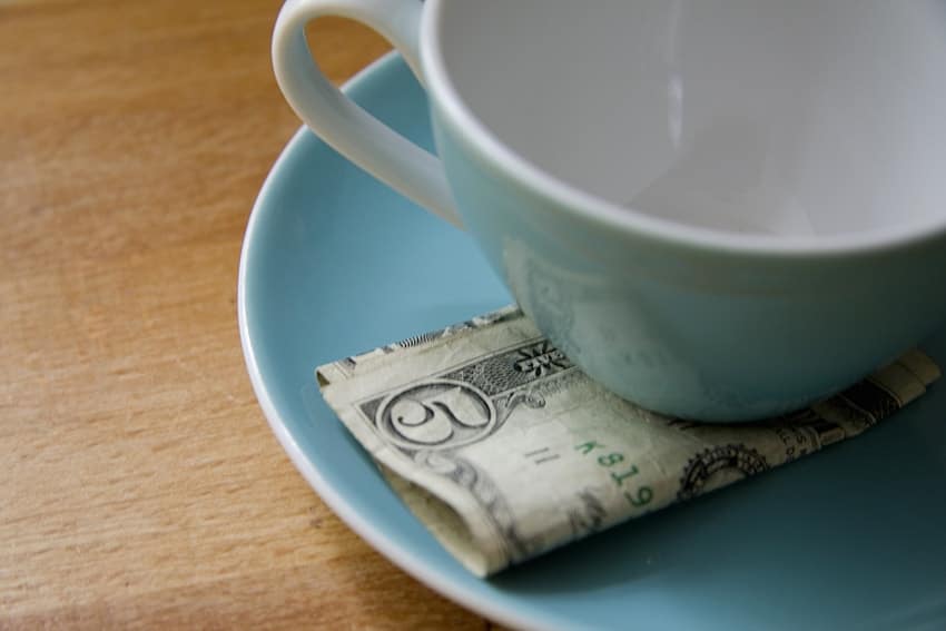 A US five dollar bill rests between a white coffee but and aqua colored plate, a tip for the waitress that served you your favorite drink. What about 5 tips to help get rid of TMJ pain?