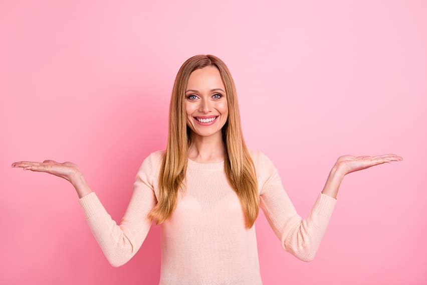 Portrait of confident, beautiful woman, isolated over pink background weighing out her option - just like deciding what is right for you; dental crowns or porcelain veneers.