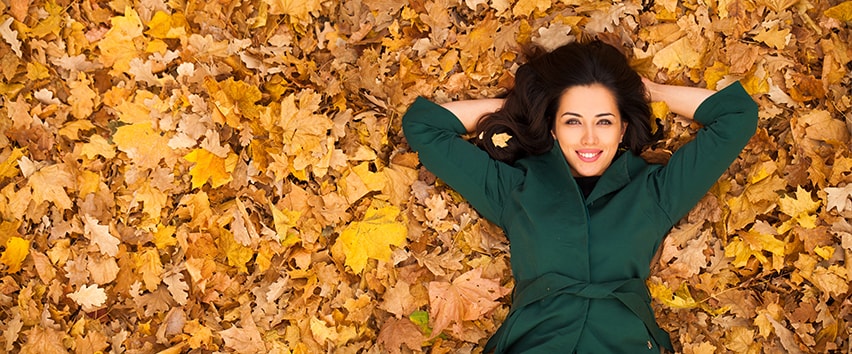 Portrait of beautiful young brunette woman laying in a park on a bed of fall leaves. Like the lovely fall day, Invisalign has given her the Perfect Orthodontic Treatment for Adults