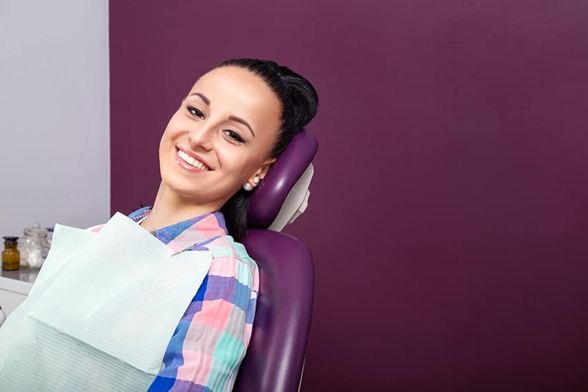 Young female dental patient in a checkered shirt relaxes at her dentist's office, ready for a checkup. Don't let the fear of the dentist make you put off cleanings. Westchester County dentists help you with all your anxiety.
