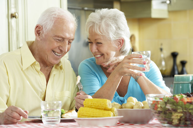 an elderly couple smiling at each other at the dinner table because they have gotten successful multiple dental implants.