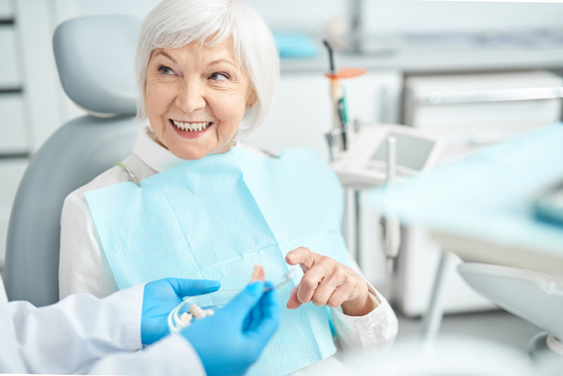 An image of an older woman sitting in a dental chair after a dental implant procedure.