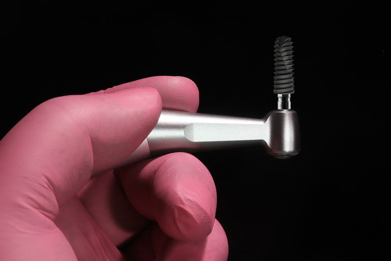 an implant being held up with a tool for placement onto the mouth