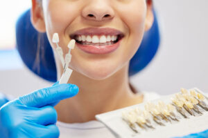 a woman getting color matched veneers while a dentist holds up the colors